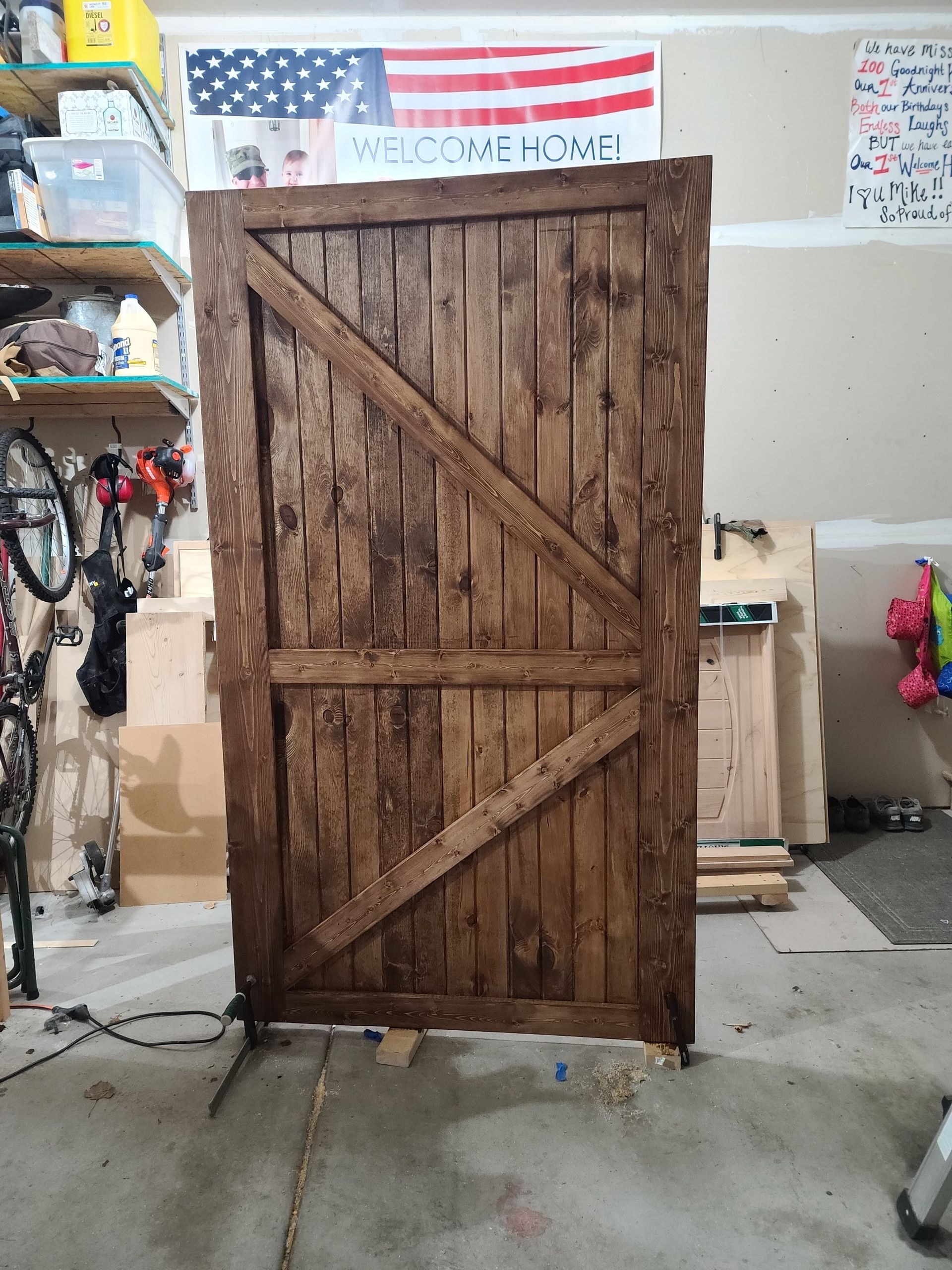 Large wooden barn door with diagonal brace, stained brown, in a garage with American flag.