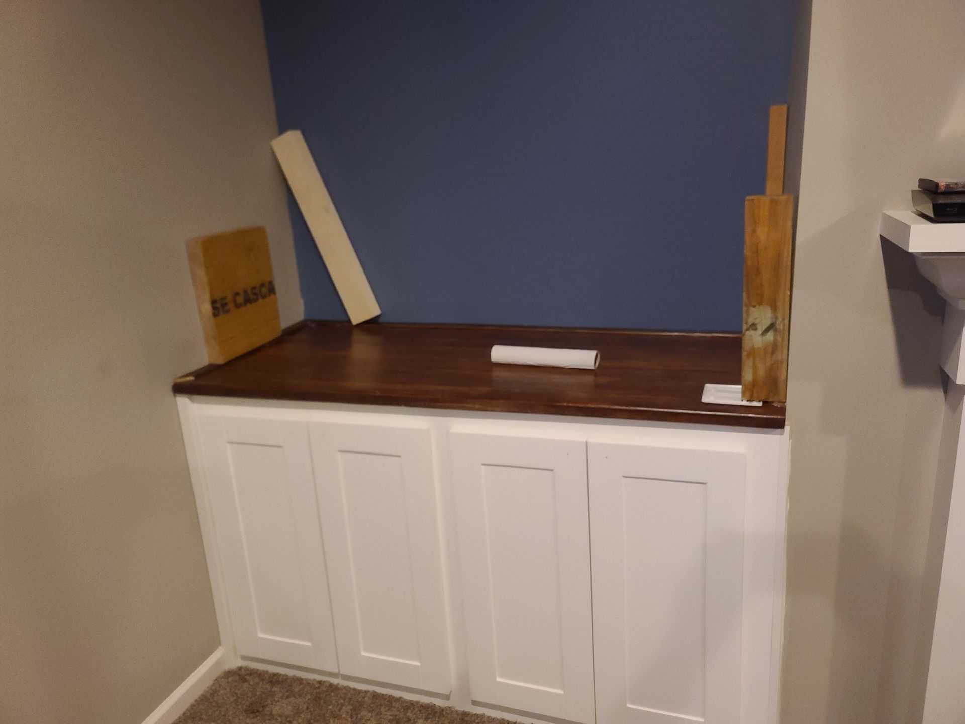 White cabinet with a dark wood countertop in a corner. A blue wall serves as the backdrop.