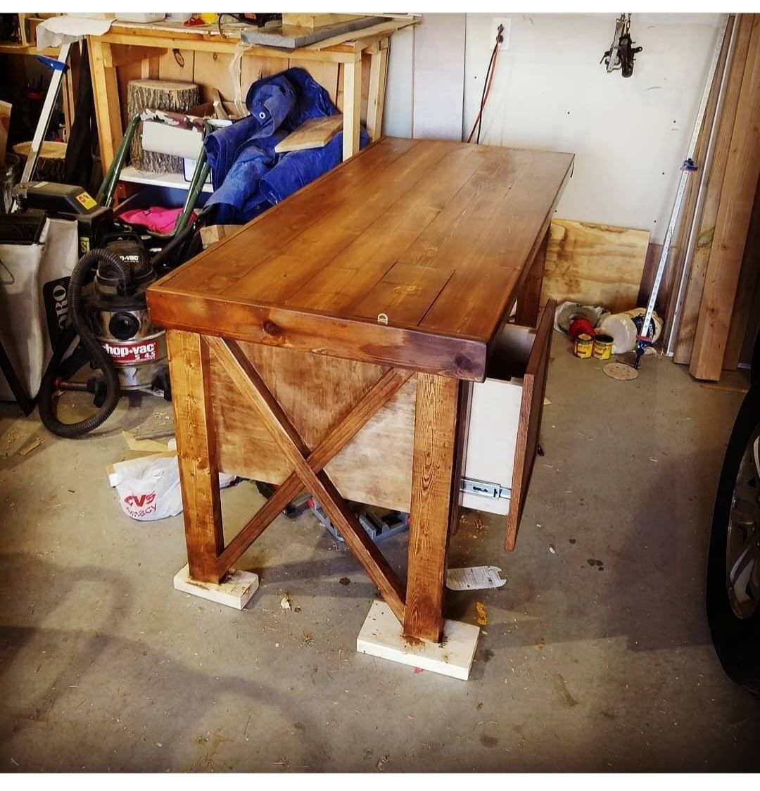 Wooden workbench with X-shaped supports in a cluttered garage, resting on blocks.