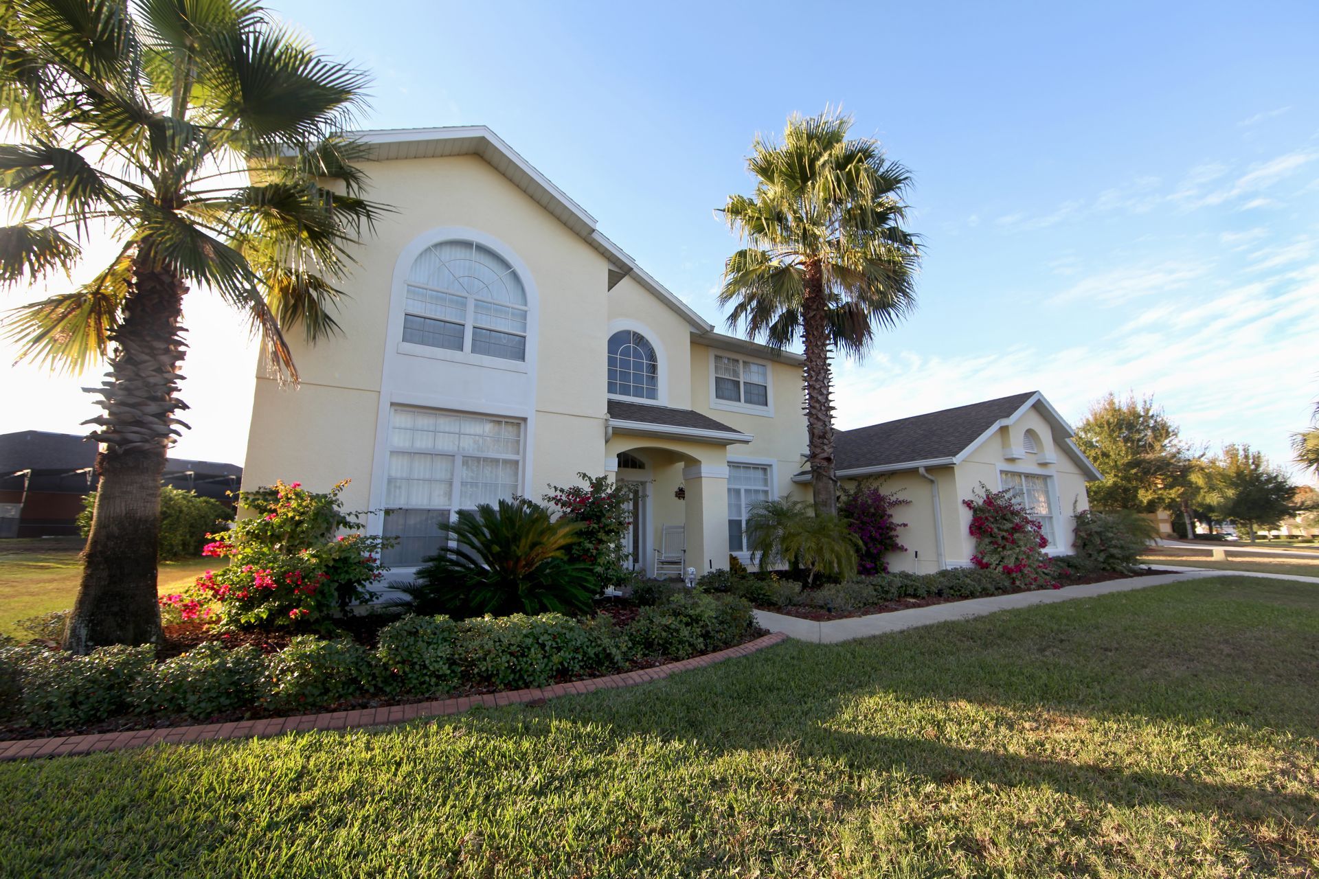 Two-story yellow house with palm trees in front