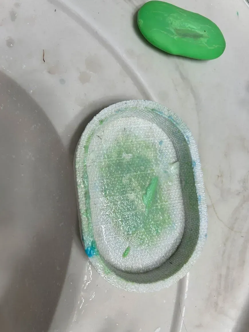 An oval, light green, glittery tray sits on a white surface next to a small, smooth, green object.