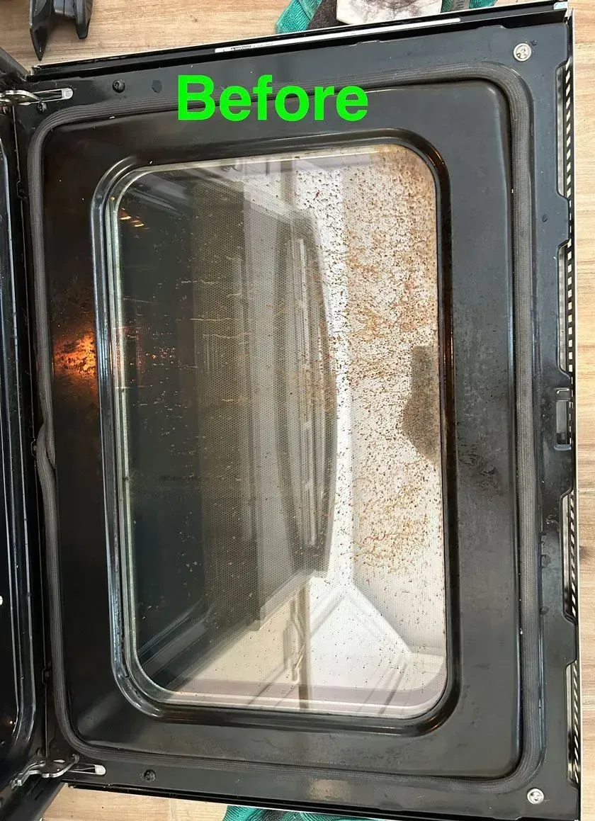 Dirty oven door with brown grease splatters on the glass, labeled with the green word 