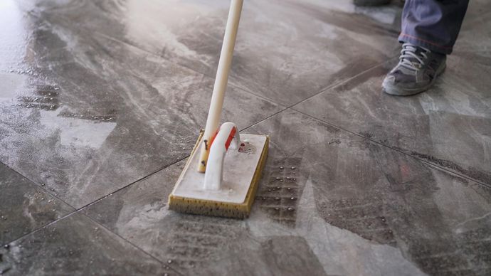 A person uses a sponge float to grout tiled flooring, smoothing the material across the gaps between the tiles.