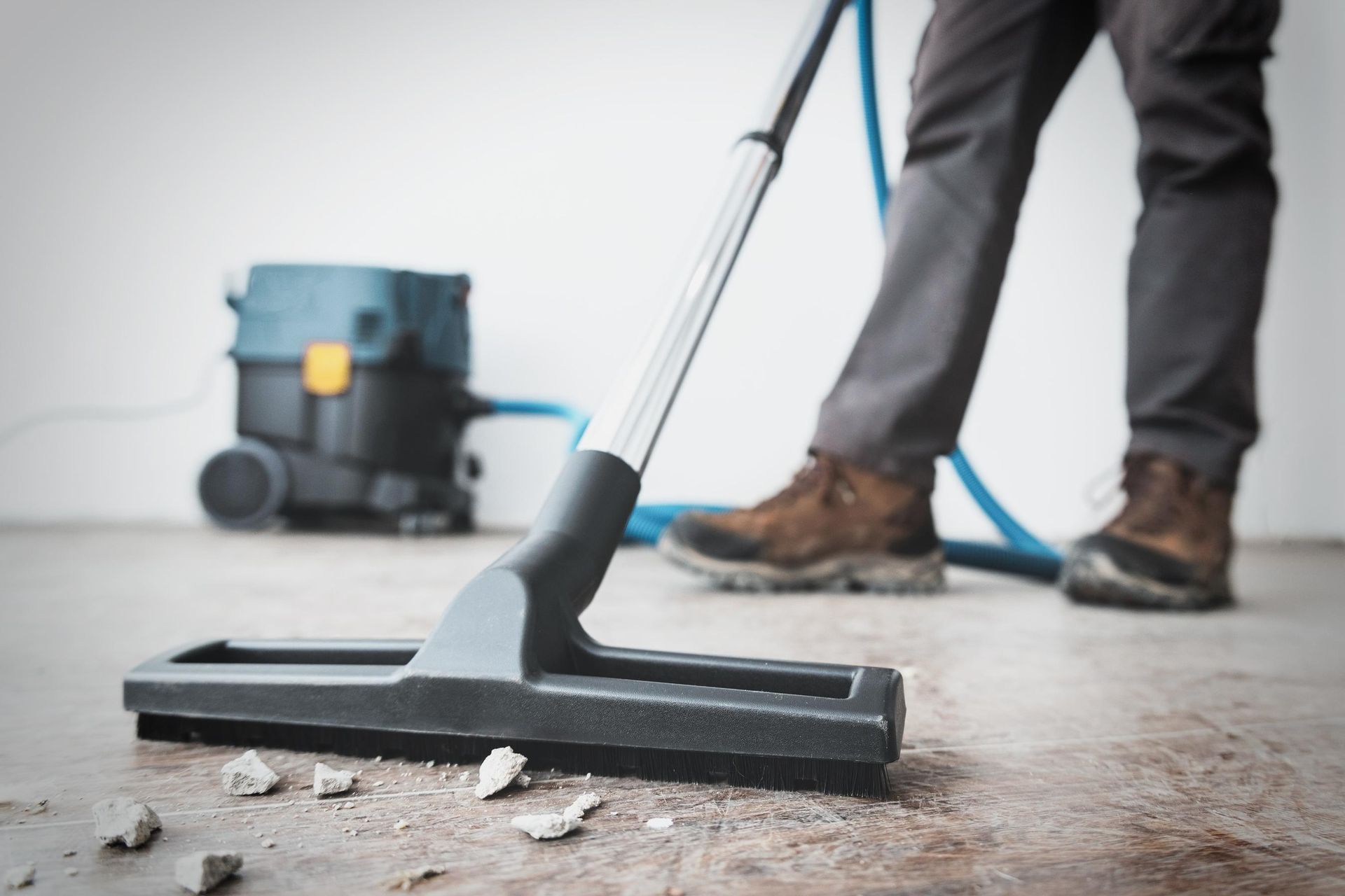 A person uses a commercial shop vacuum to clean construction debris from a concrete floor.