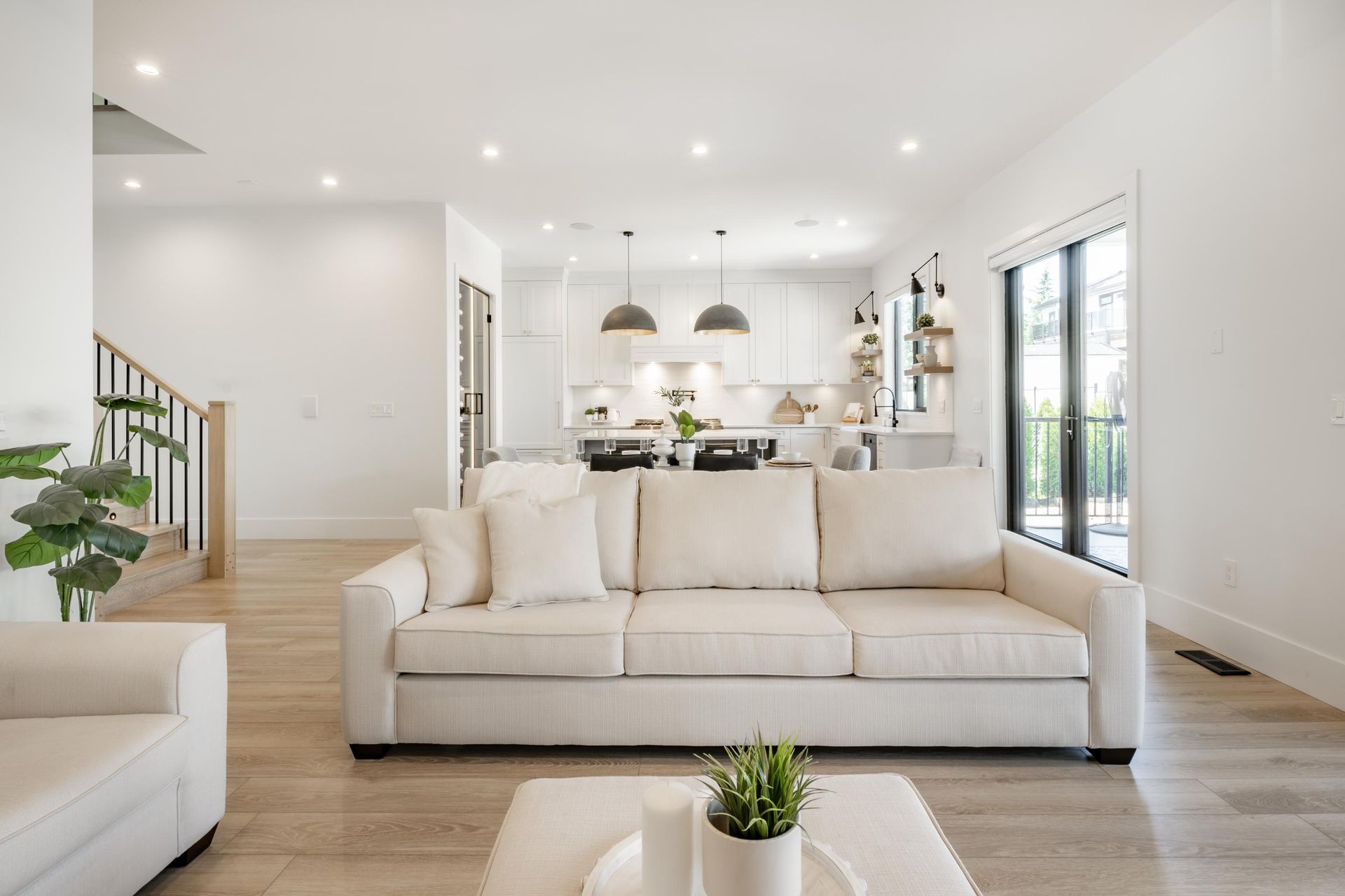 A bright, modern living room with a beige sofa, hardwood floors, and an open-concept kitchen in the background.