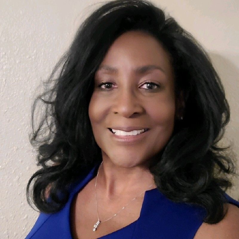 A woman wearing a blue shirt and a necklace is smiling for the camera.