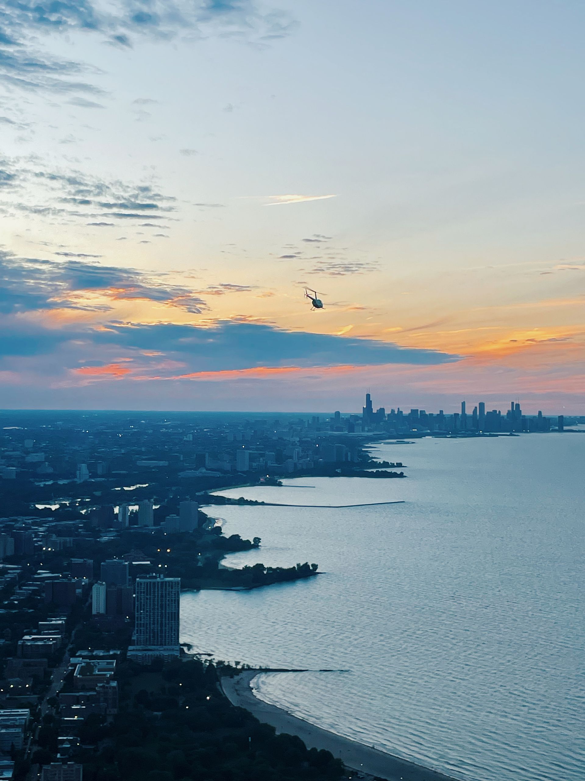 City skyline at sunset with a helicopter flying over the lake.