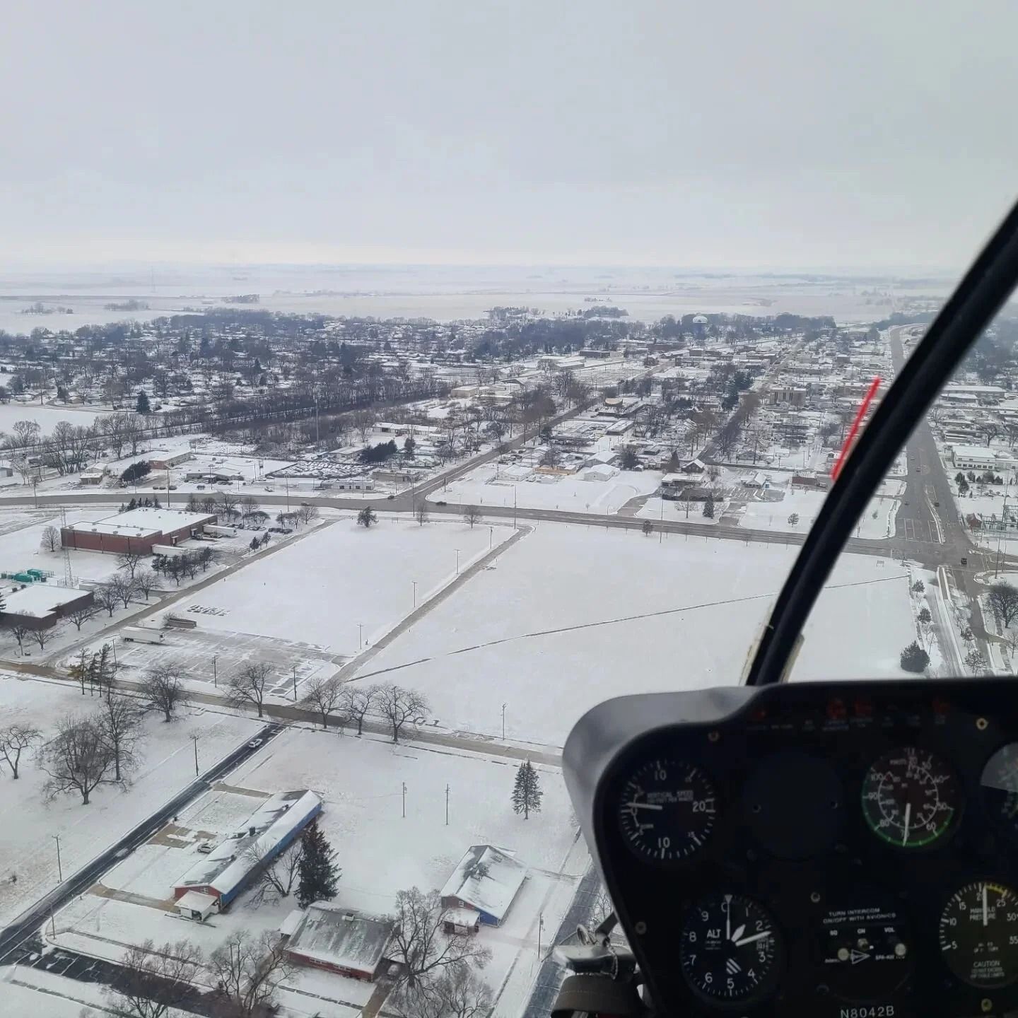 Helicopter view of a snow-covered town. Gauges visible in foreground. Cloudy sky overhead.