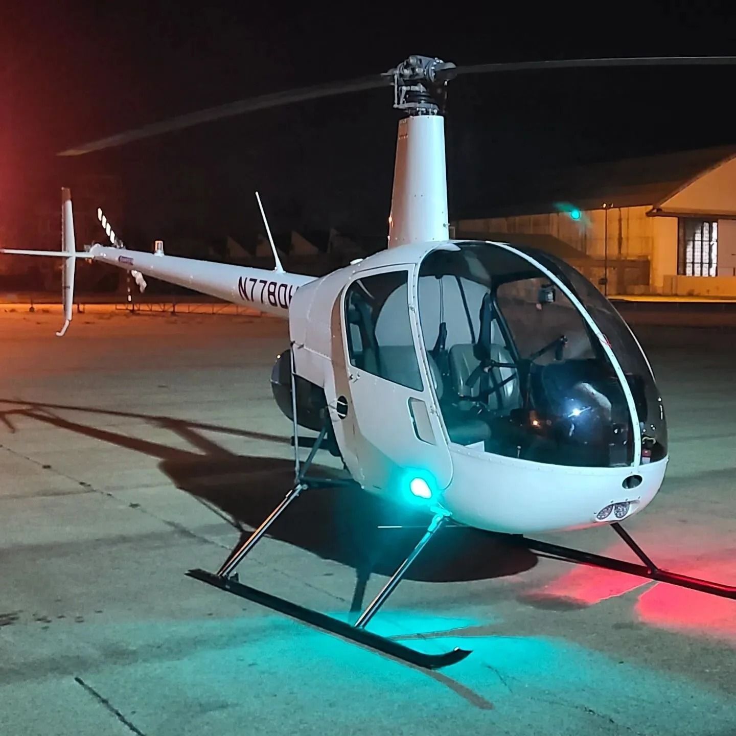 White helicopter on the ground at night with blue and red lights.  The tail reads N7780H.