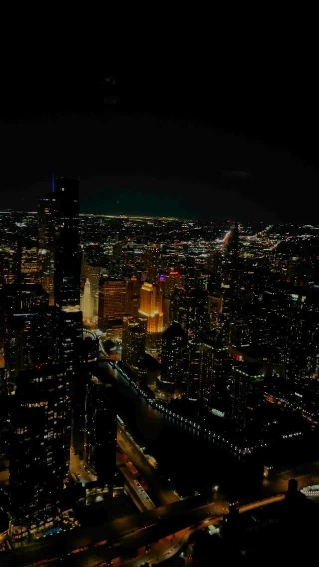 Nighttime cityscape with glowing lights, dark silhouettes of buildings against the night sky.