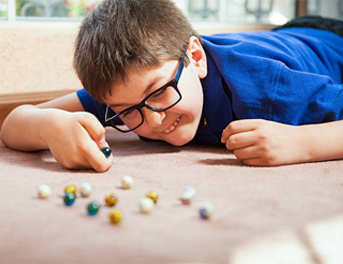 a young boy wearing glasses is laying on the floor playing with marbles