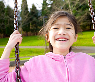 a little girl is sitting on a swing in a park and smiling