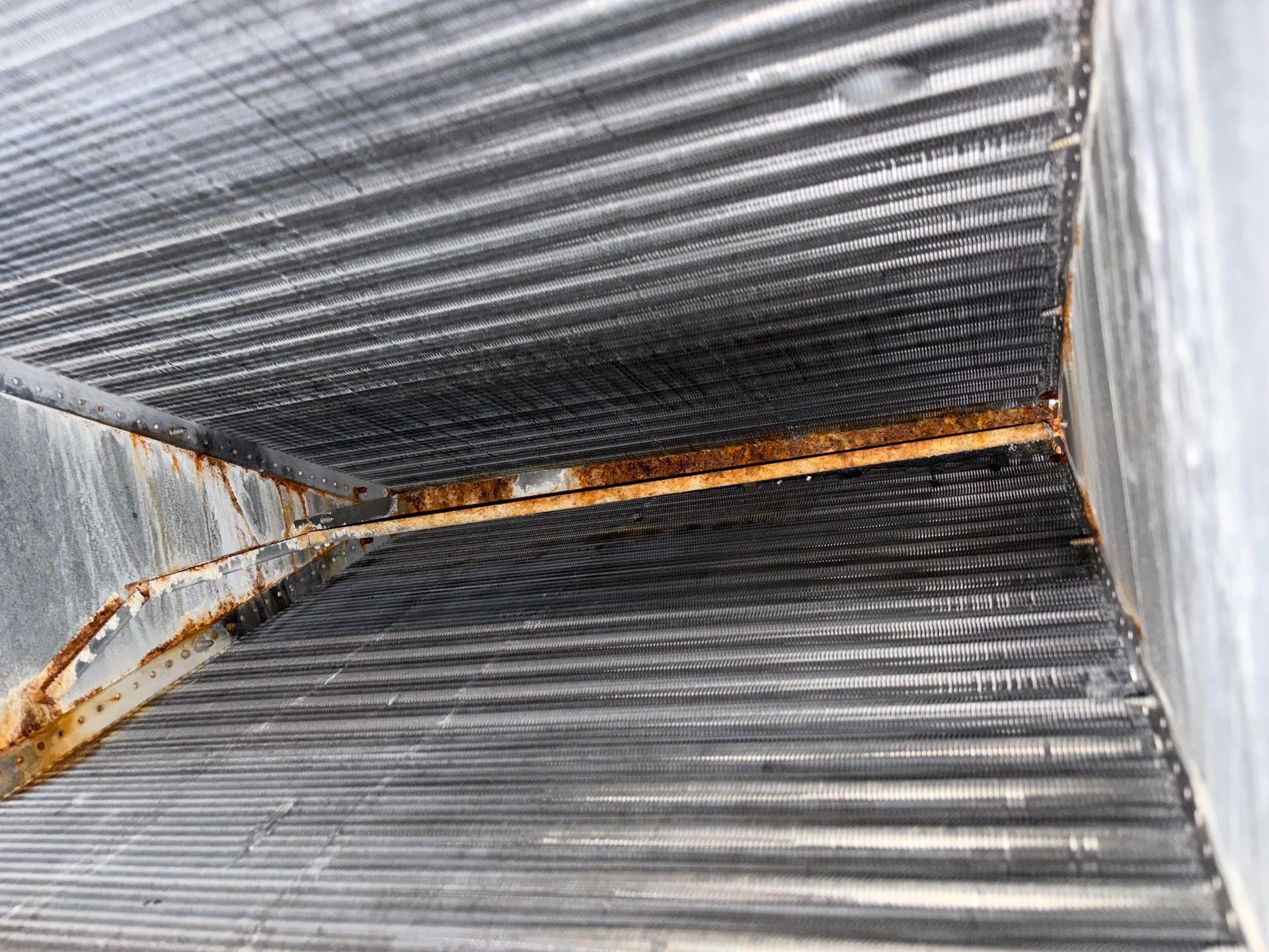 Rusty corrugated metal duct interior with a diagonal seam and rust stains