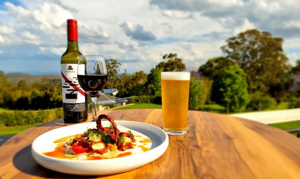 A Bottle of Wine, a Glass of Beer and a Plate of Food on a Wooden Table — Monty Brewing Co. In Highfields, QLD