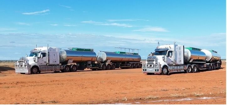 Three Semi Trucks Are Parked In Front Of A Blue Building — Willow's Bitumen Haulage Pty Ltd In Stuart, QLD