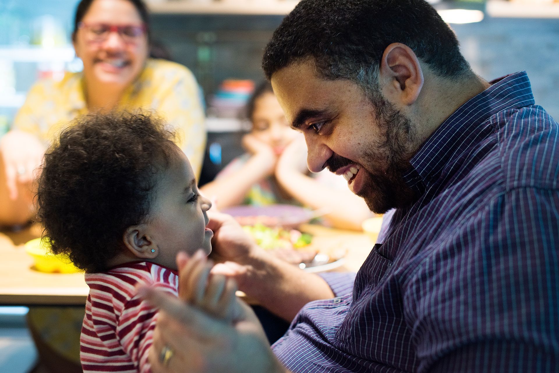 A man is holding a baby in his arms while sitting at a table.