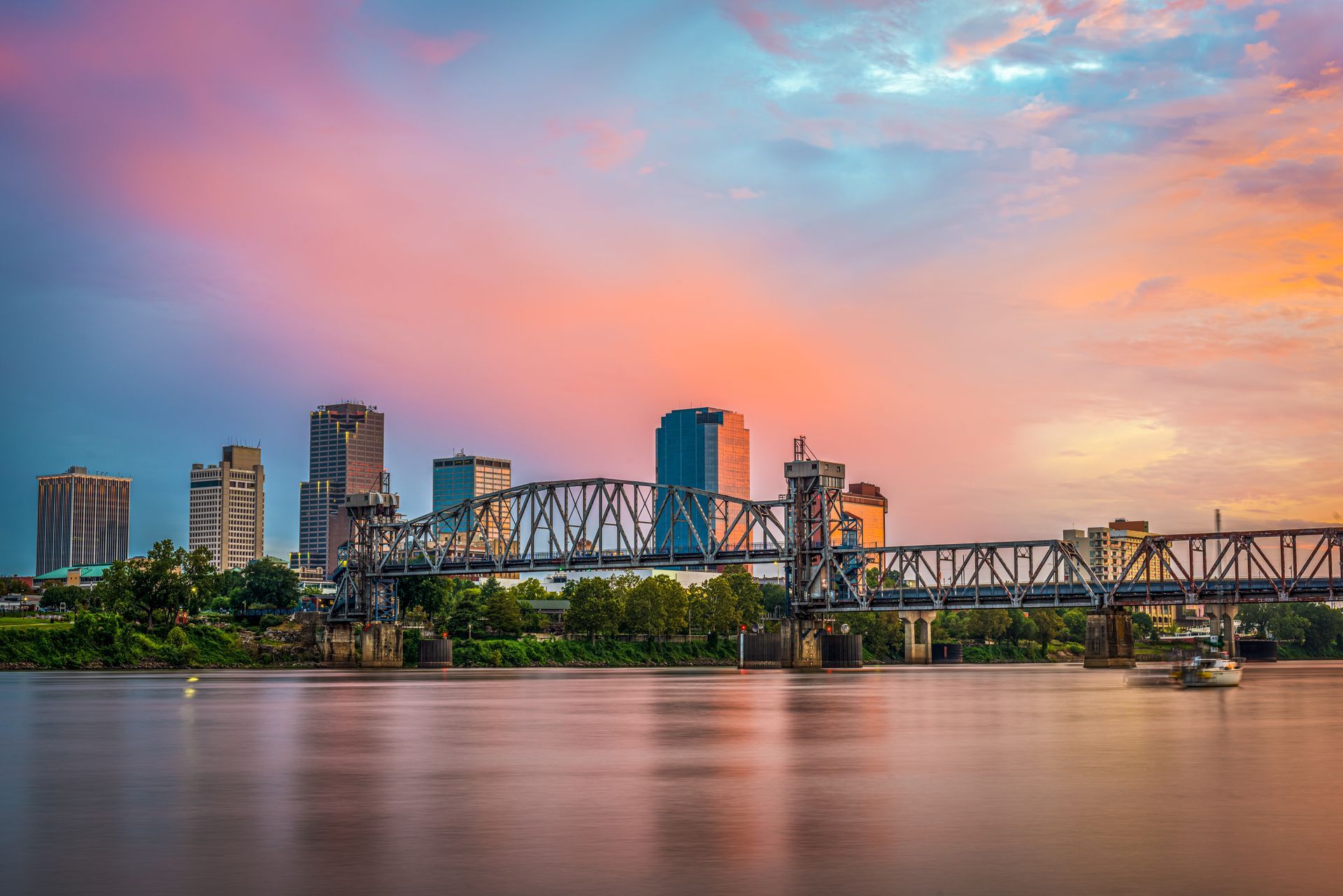 A bridge over a river with a city skyline in the background at sunset.