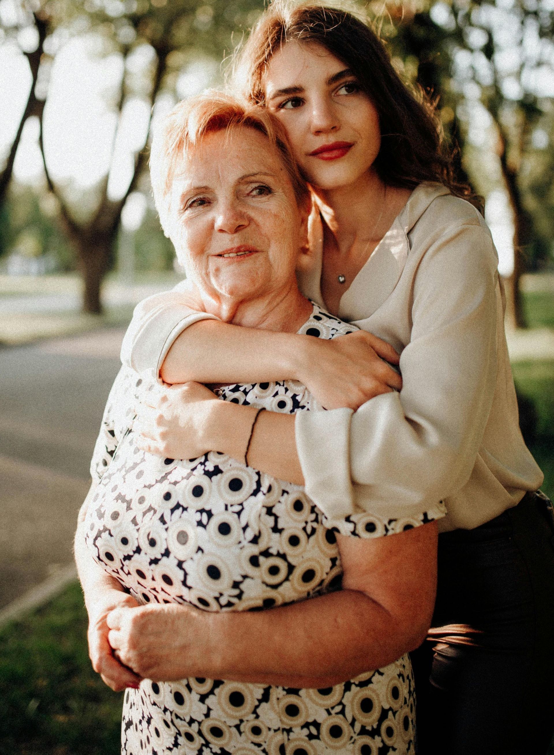 A young woman is hugging an older woman in a park.