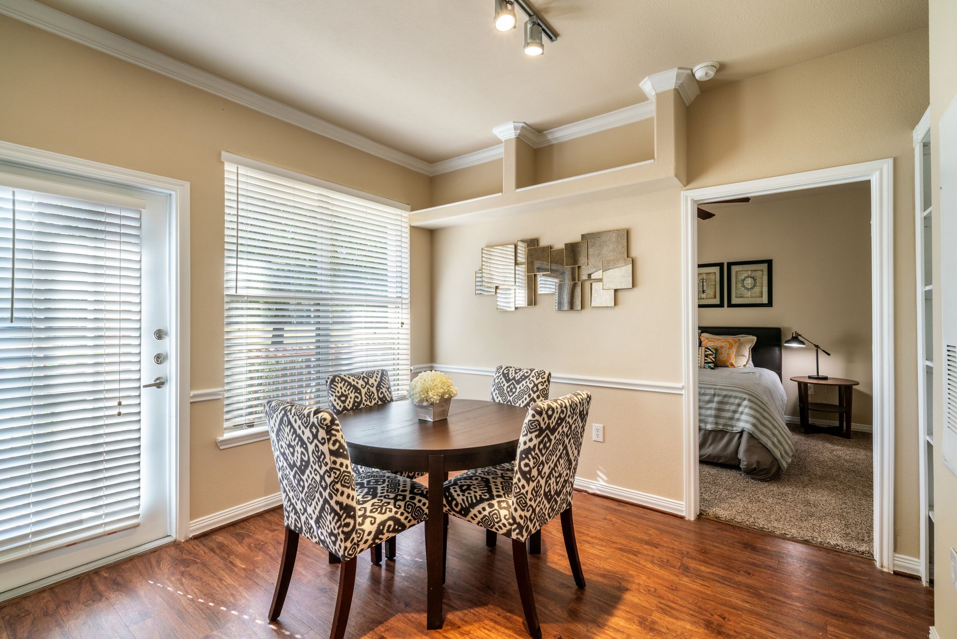 Dining area with round table, patterned chairs, and a view into a bedroom.