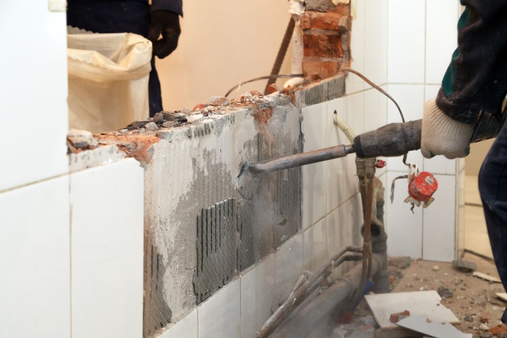 Worker uses a jackhammer to break a tiled wall during demolition.
