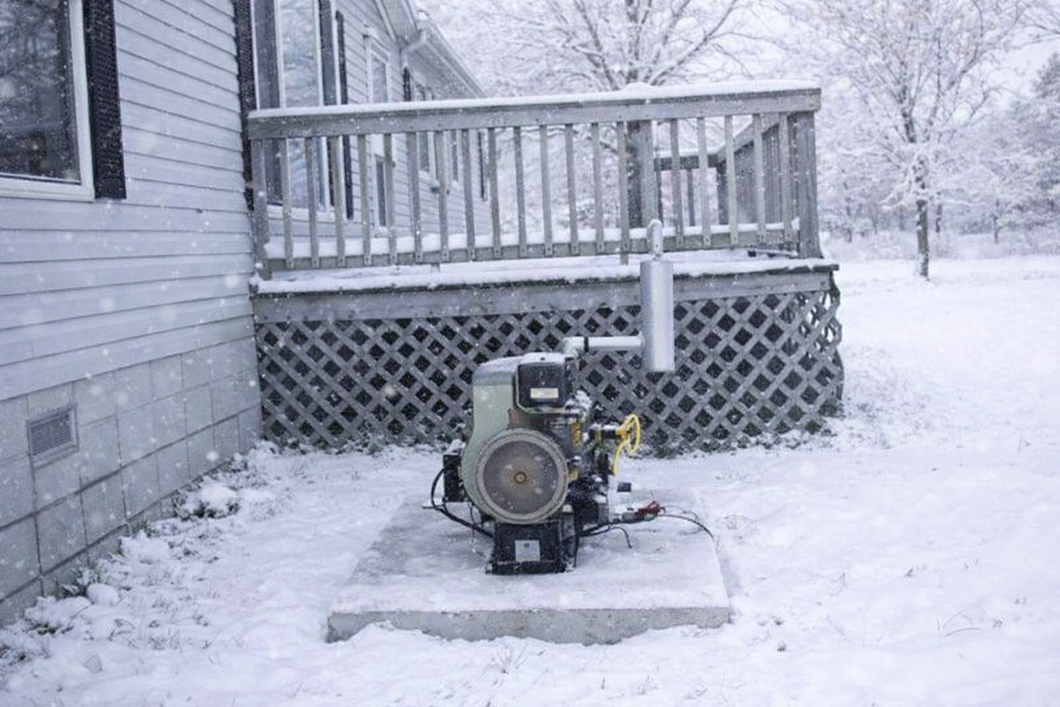 Generator next to a house deck in snowy weather.