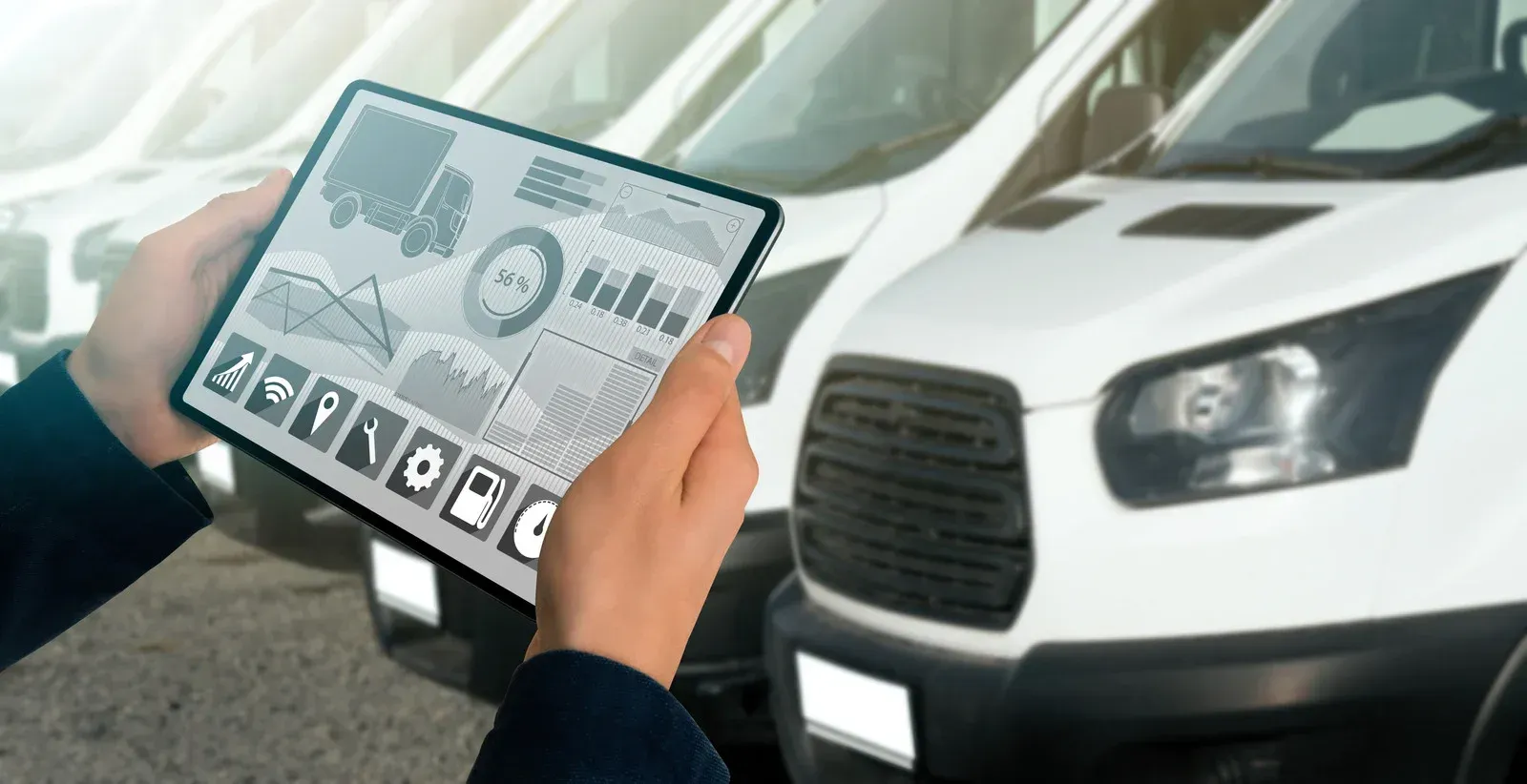 A person holds a tablet displaying fleet management analytics in front of a row of white delivery vans.
