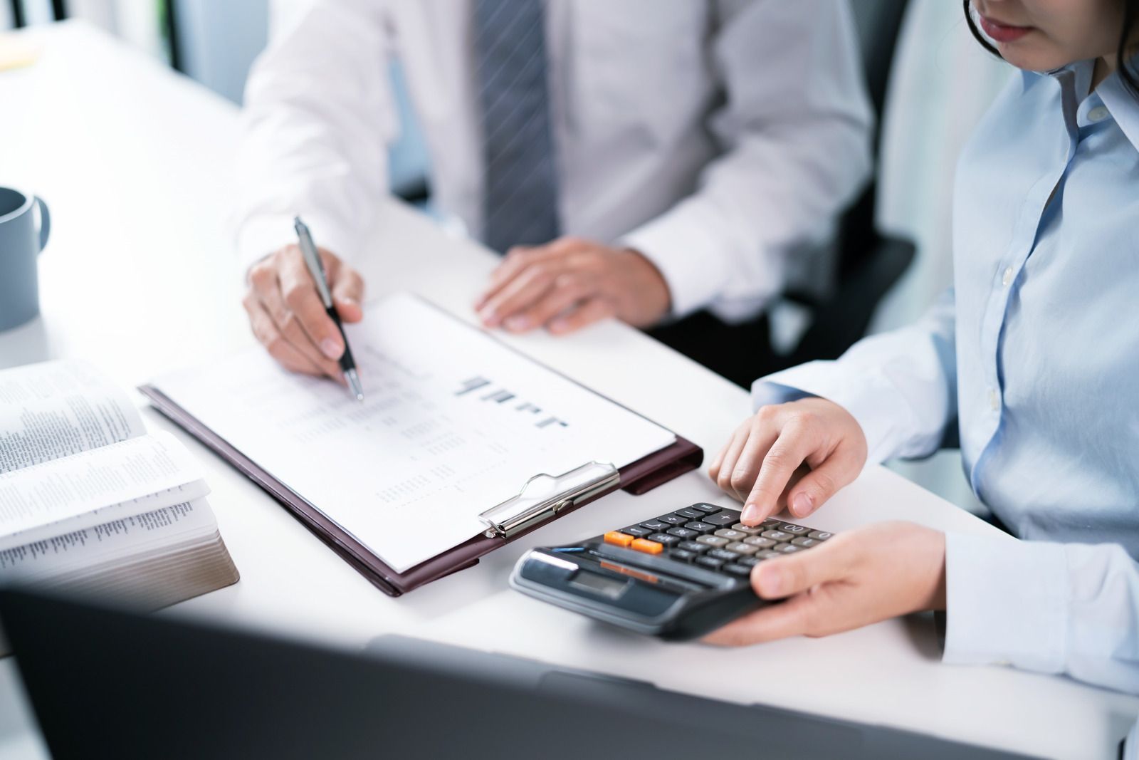 Two professionals in business attire at a desk, one writing on a document while the other uses a calculator.