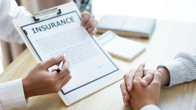 A professional discusses an insurance document with a client at a desk, pointing to the paperwork with a pen.