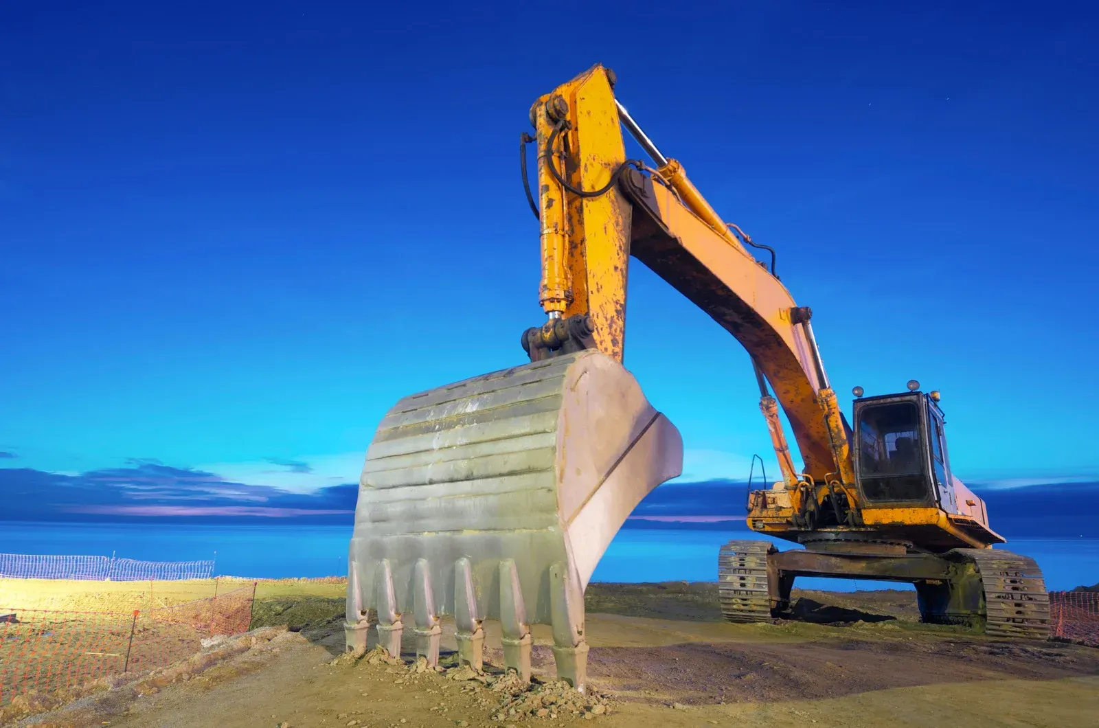 Worker in a yellow hard hat and safety vest holds a tablet while overlooking a large industrial port with cranes.