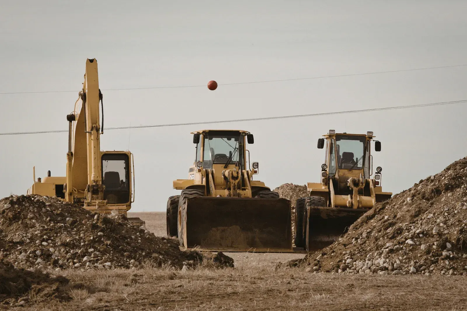 A small model house with a white exterior and red roof is sheltered beneath a large, open red umbrella.