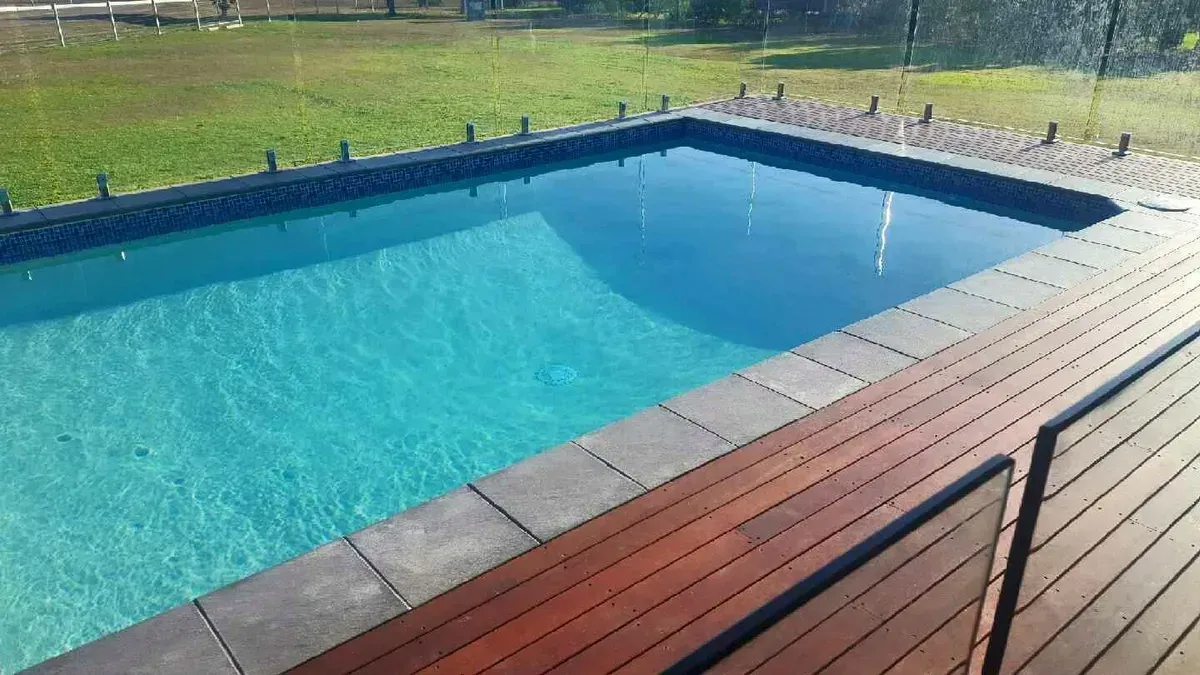 A Swimming Pool With A Wooden Deck Surrounding It — Tropical North Swimming Pools 'n' Spas In Currajong, QLD