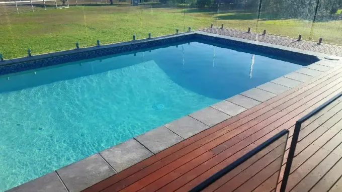 A Swimming Pool With A Wooden Deck Surrounding It — Tropical North Swimming Pools 'n' Spas In Currajong, QLD
