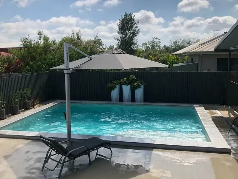 A Large Swimming Pool With A Large Umbrella And Chairs Around It — Tropical North Swimming Pools 'n' Spas In Currajong, QLD