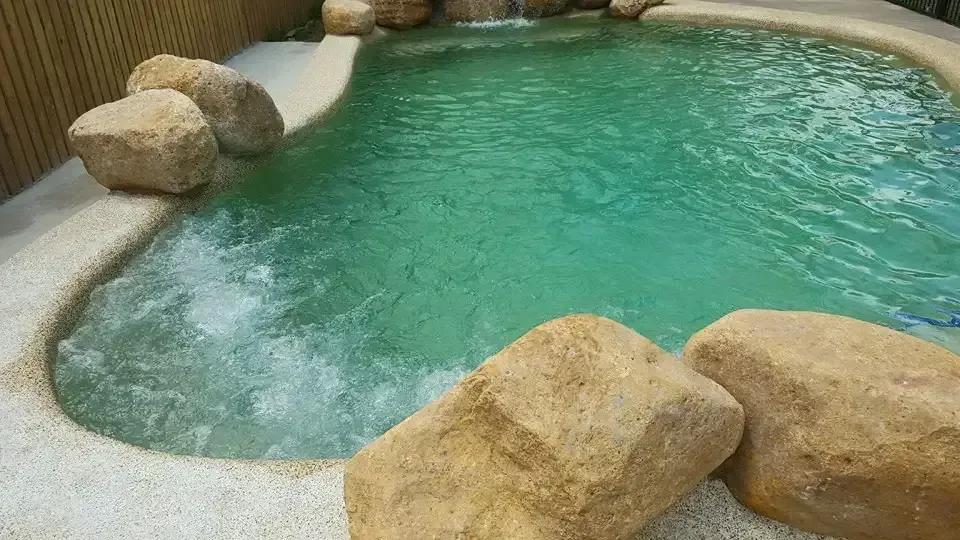 A Large Swimming Pool Surrounded By Rocks And A Waterfall — Tropical North Swimming Pools 'n' Spas In Currajong, QLD