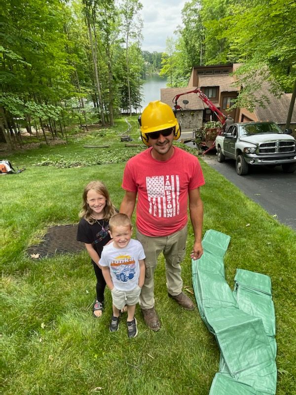 A man wearing a hard hat is standing next to two children in a yard.
