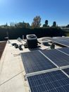 Solar panels on a rooftop under a clear blue sky, with HVAC units and trees in the background