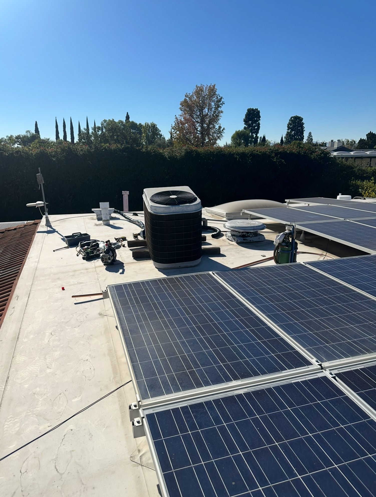Solar panels installed on a rooftop under a clear blue sky, with HVAC units nearby.