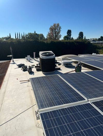 Solar panels on a flat rooftop under a clear blue sky, with HVAC units and trees in the distance.