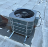 Outdoor rooftop air conditioning unit with a top fan and attached hose on a concrete surface