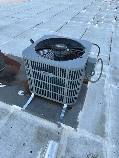 Outdoor air conditioning unit on a flat rooftop, with snow on the ground around it.