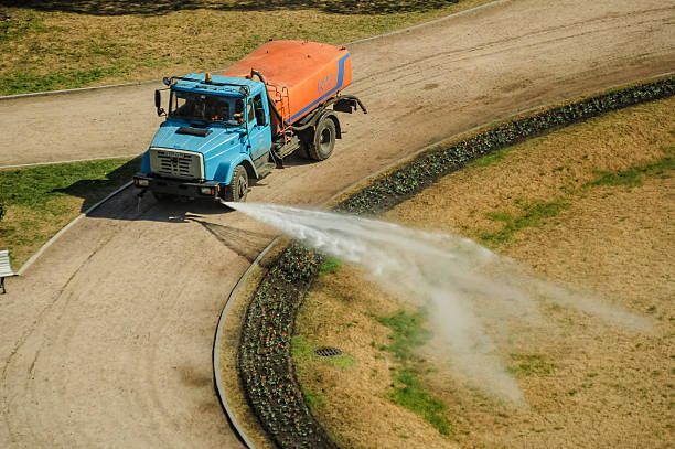 Workers performing hydroseeding and landscaping on a sloped rural hillside.