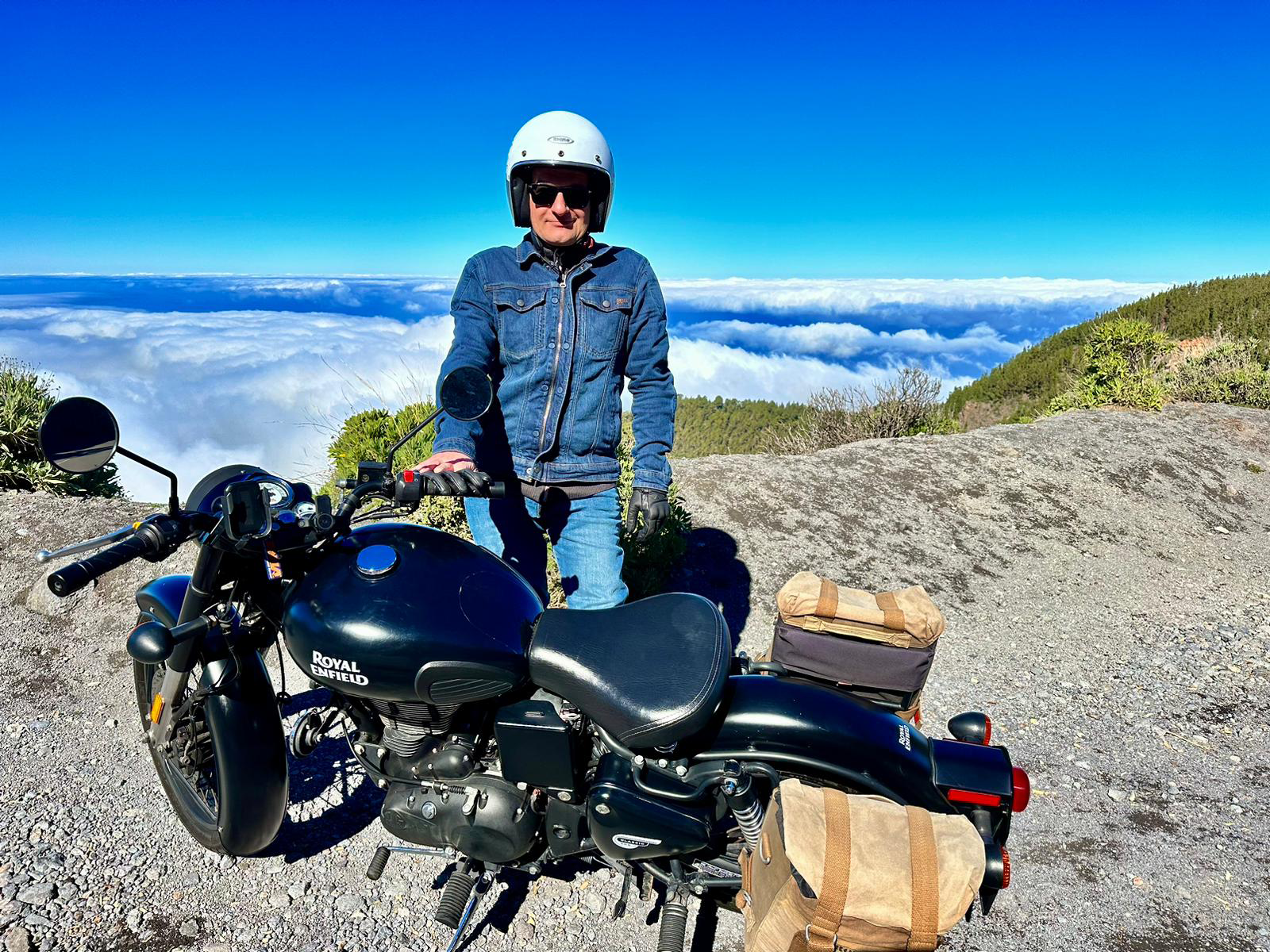 A man is standing next to a motorcycle on top of a mountain.