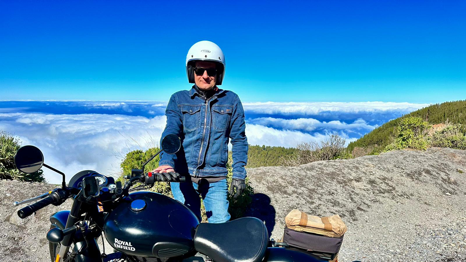 A man is standing next to a motorcycle on top of a mountain.