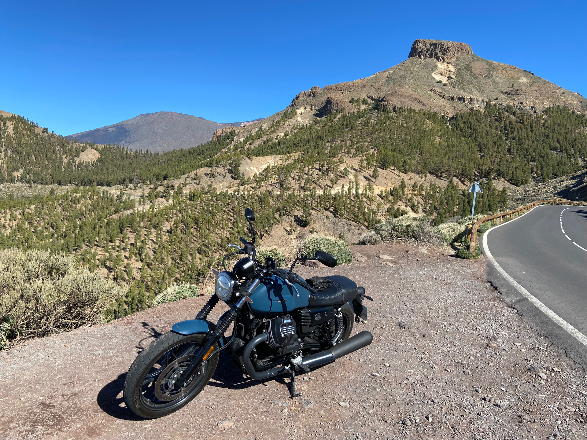A motorcycle is parked on the side of a road next to a mountain.