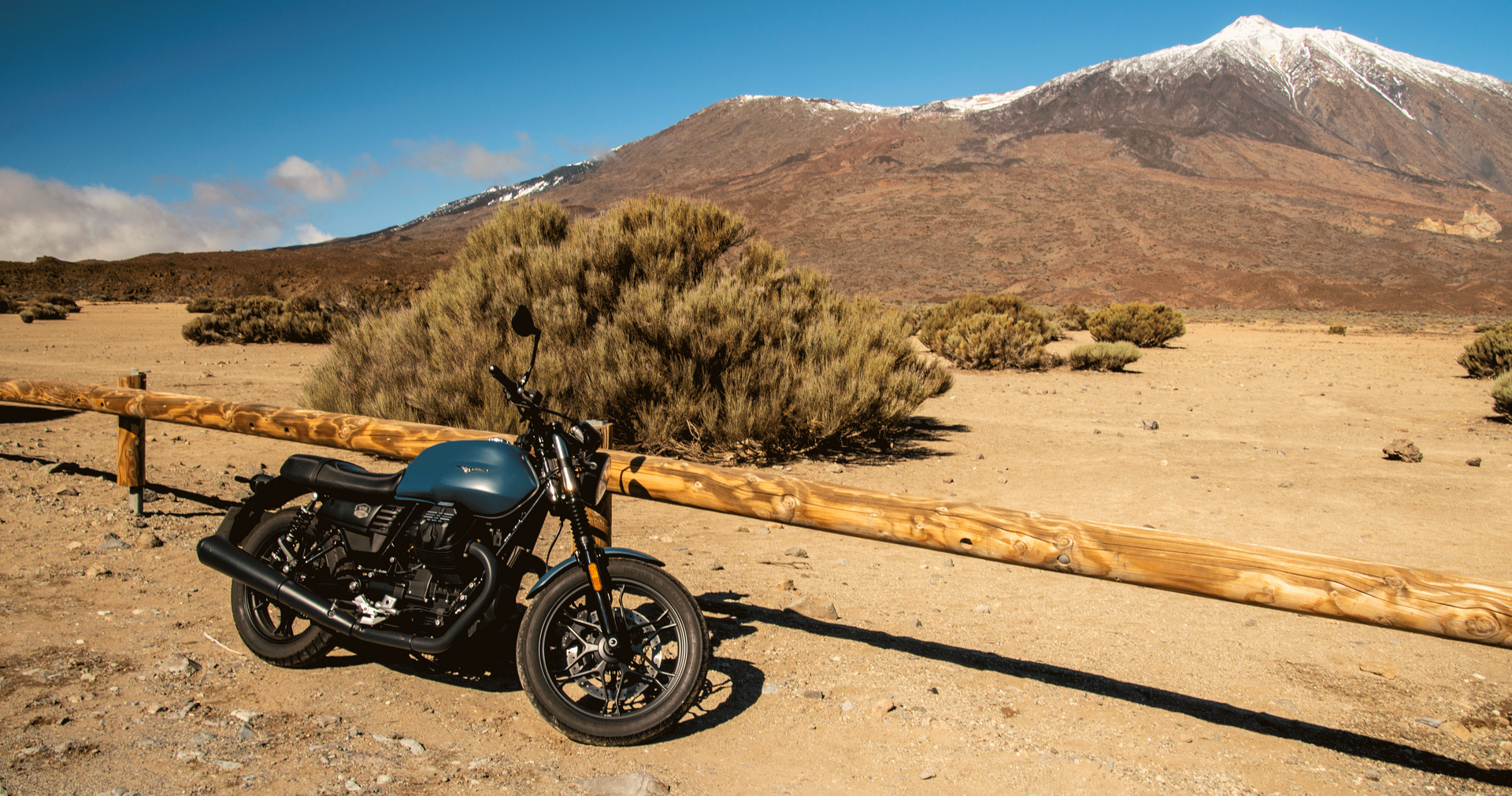 A motorcycle is parked in the desert next to a wooden fence.