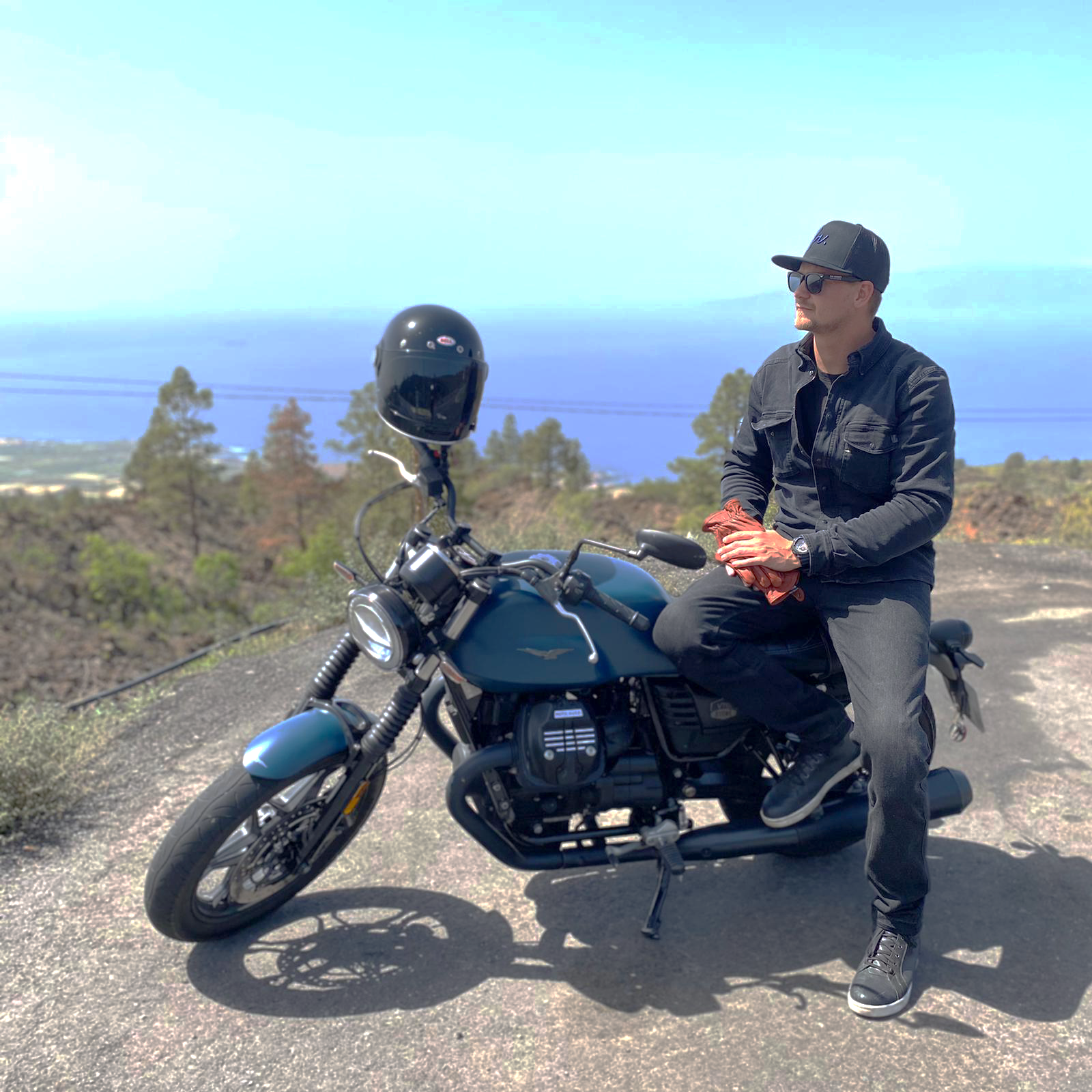 A man is sitting on a motorcycle with a view of the ocean behind him