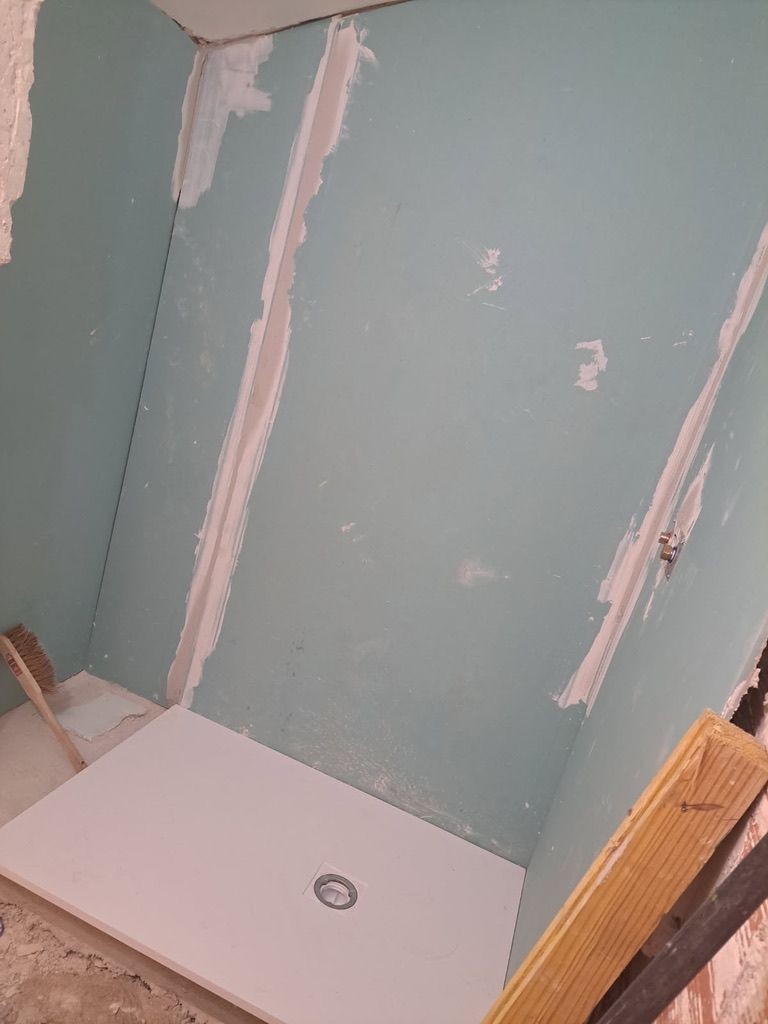 Cabine de douche en construction, avec cloisons sèches bleues et base blanche.