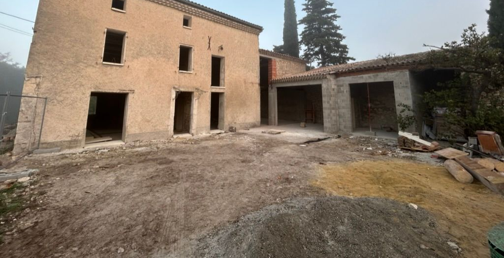 Vieille maison en pierre en rénovation, avec garage, sur fond de ciel brumeux.
