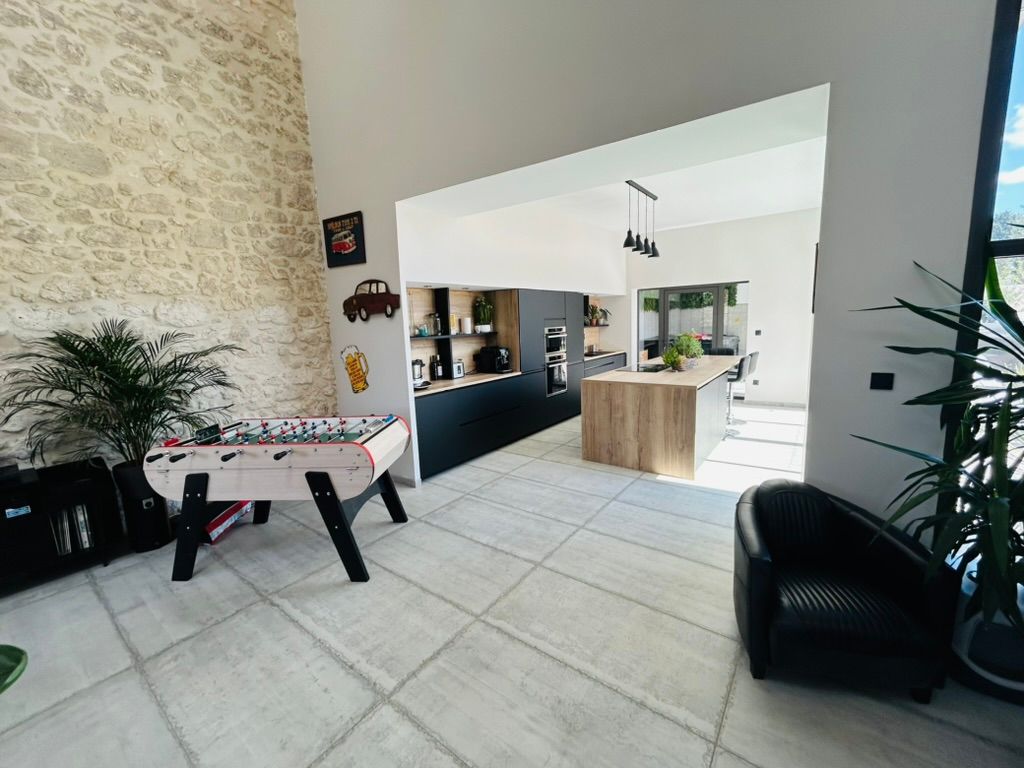 Intérieur moderne avec un baby-foot, donnant sur une cuisine avec un îlot en bois clair et des placards noirs.