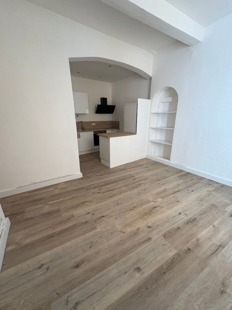 Vue intérieure : parquet clair, murs blancs, cuisine avec arche, étagères intégrées.